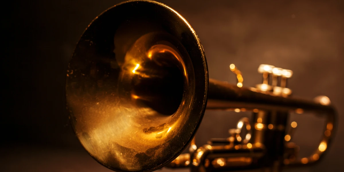 Close-up of a golden trumpet against a dark background. The valves and lead pipe are visible, and the bell is pointed slightly upwards.