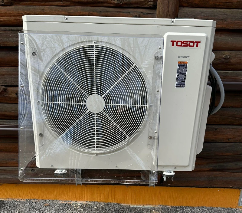 A white air conditioning heat pump unit with a wind baffle mounted on a wooden wall, illustrating a contemporary approach to home climate control.